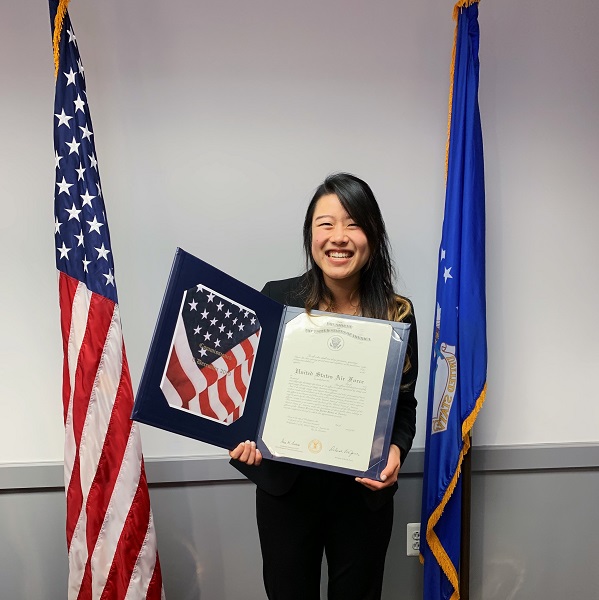 Elizabeth Lee, a physician assistant student, standing next to American flag with notification of Air Force scholarship.